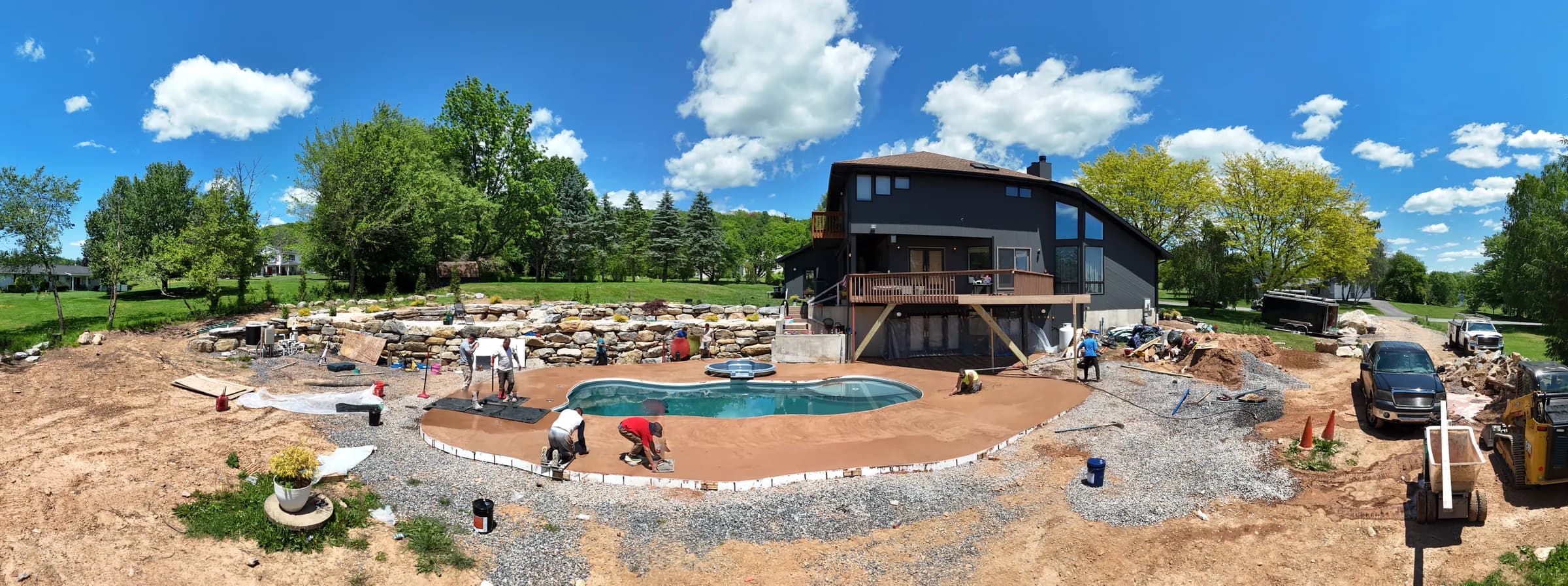 Wide aerial of a backyard pool and home under construction on a sunny day